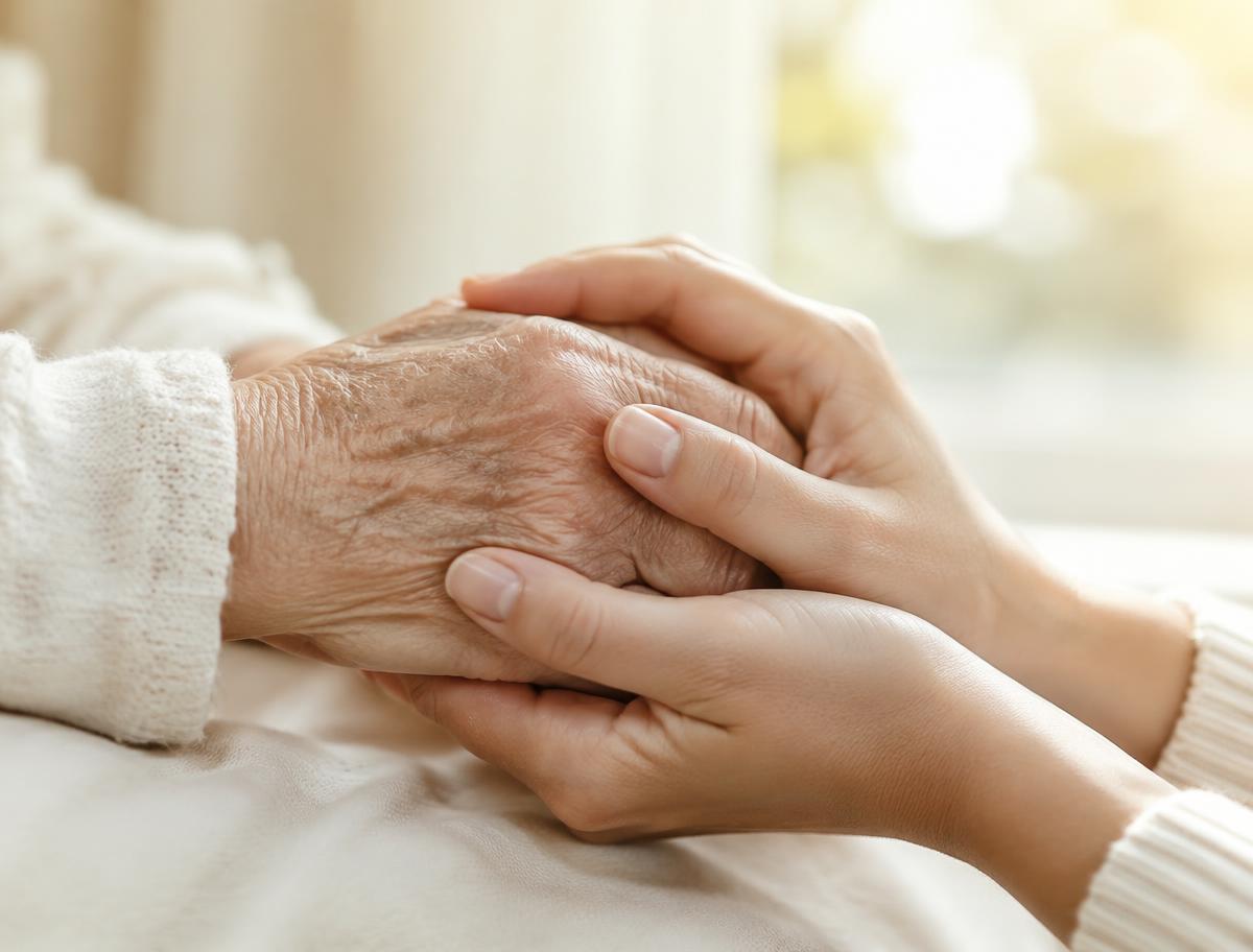 A younger person gently holding an older person's hand in comfort